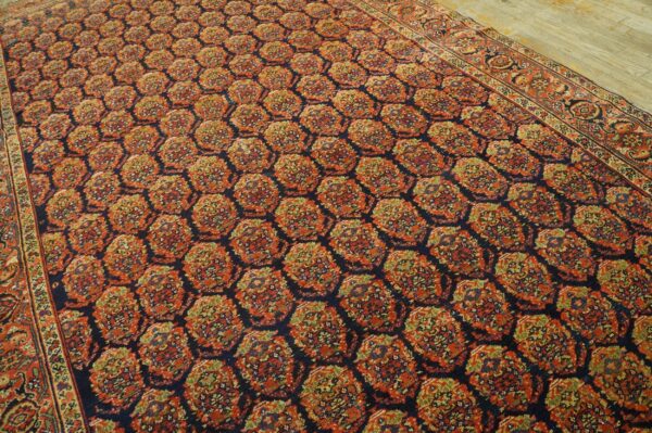 Navy rug featuring a dense, repeating pattern of red and olive green stylized medallions on wood flooring.