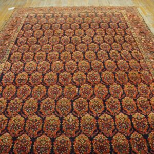 Ornate navy rug featuring a repeating rust and gold medallion pattern on rustic yellow hardwood flooring.