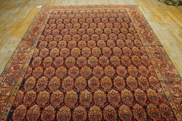 Ornate navy rug featuring a repeating rust and gold medallion pattern on rustic yellow hardwood flooring.