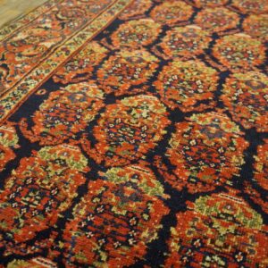 Close-up of a terracotta and navy repeating medallion rug resting on rustic wood flooring.