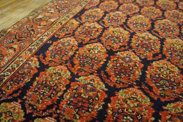 Close-up of a terracotta and navy repeating medallion rug resting on rustic wood flooring.