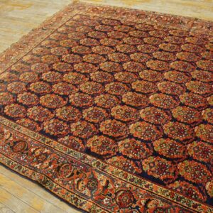 Navy and rust patterned rug with repeating floral medallions lying on rustic, wide plank wood flooring.