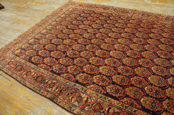 Navy and rust patterned rug with repeating floral medallions lying on rustic, wide plank wood flooring.