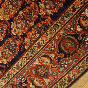 Red, navy, and gold traditional rug pattern with an intricate border resting on bright yellow wood flooring.