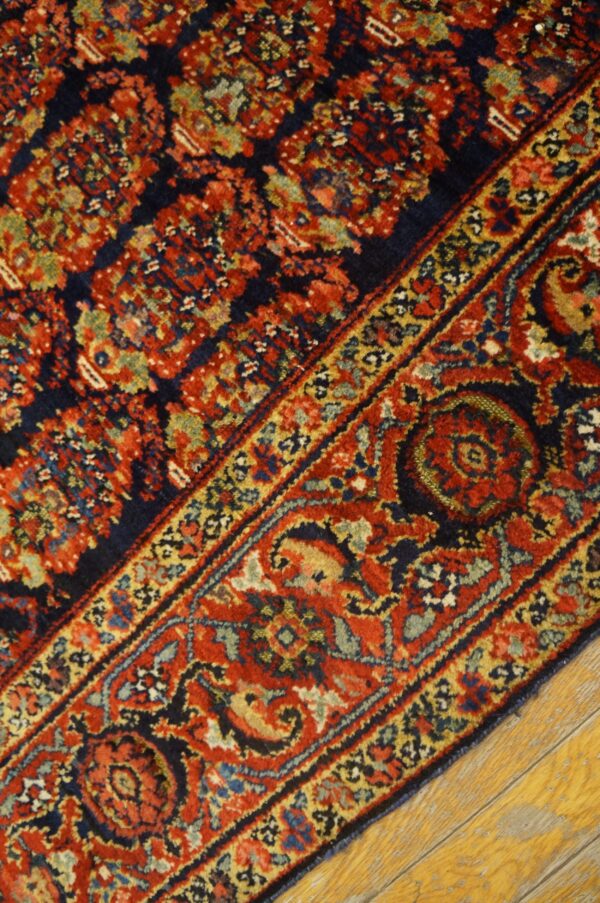 Red, navy, and gold traditional rug pattern with an intricate border resting on bright yellow wood flooring.