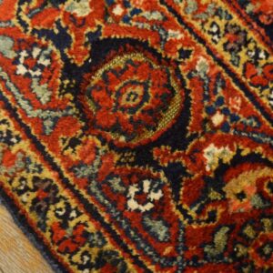 Ornate, medium-pile rug detail showing red, navy, teal, and yellow intricate patterns on light wood planks.