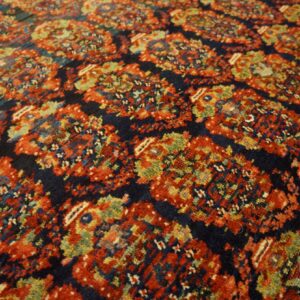 Intricate traditional rug pattern with dark blue ground, highlighting red, olive green, and gold details.