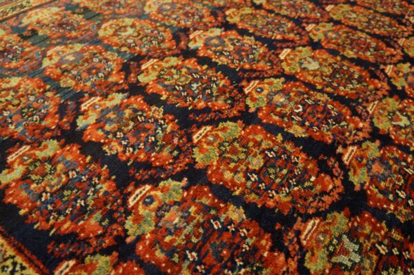 Intricate traditional rug pattern with dark blue ground, highlighting red, olive green, and gold details.