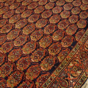 Intricate red, navy, and green patterned rug with a wide border on whitewashed wooden floorboards.
