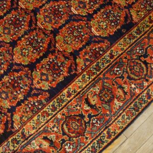 Close-up of a navy and red patterned rug with detailed borders on light rustic wooden planks.