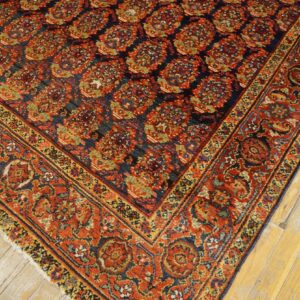 Intricate traditional rug featuring a dark blue field, rust motifs, and an elaborate border on distressed wood flooring.