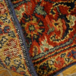 High-pile red and blue patterned rug folded to expose its golden, tightly woven backing on wood flooring.