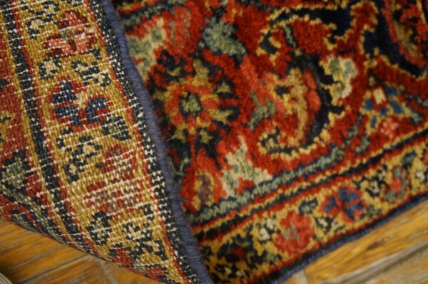 High-pile red and blue patterned rug folded to expose its golden, tightly woven backing on wood flooring.