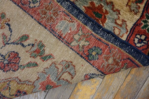 Detailed woven rug backing in red, blue, and beige patterns is curled, showing the high pile on a wood floor.