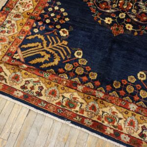 A navy blue traditional rug with gold, red, and cream floral borders sits on distressed light wood floors.