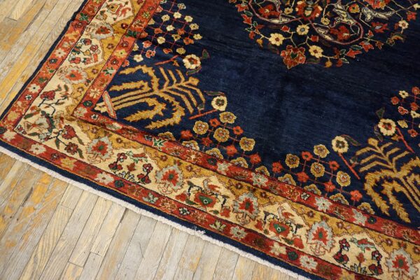 A navy blue traditional rug with gold, red, and cream floral borders sits on distressed light wood floors.