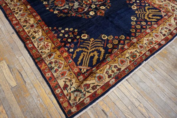 Ornate navy blue rug with dense floral patterns in cream, red, and gold, lying on rustic wood flooring.