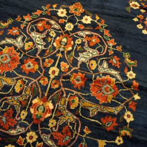 Intricate floral and stylized bird motifs in orange and gold cover the textured dark blue rug field.