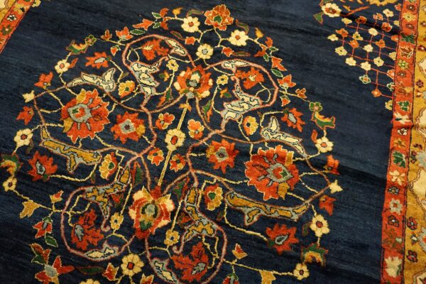 Intricate floral and stylized bird motifs in orange and gold cover the textured dark blue rug field.