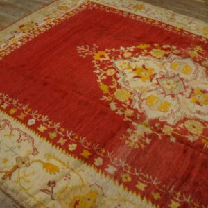 Red rug with a large cream and yellow medallion pattern on weathered wood floors.