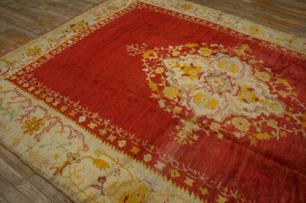 Red rug with a large cream and yellow medallion pattern on weathered wood floors.