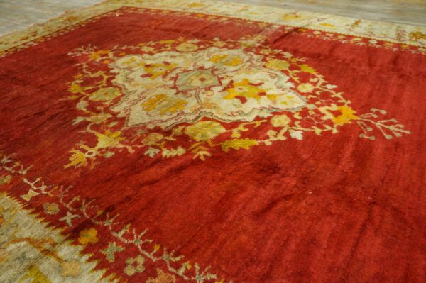 Deep red high-pile rug with an ornate central medallion in cream, gold, and muted green on light flooring.