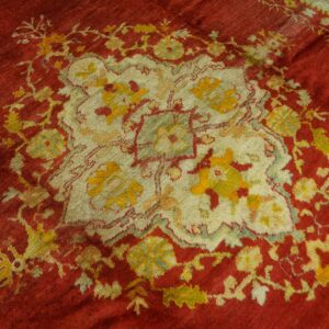 Low pile rug with a red field surrounding a stylized cream, yellow, and green floral center.