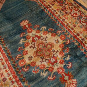 Textured blue rug with a central floral medallion and multi-colored red and cream striped borders on wood floor.