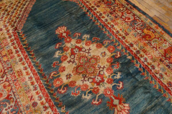 Textured blue rug with a central floral medallion and multi-colored red and cream striped borders on wood floor.