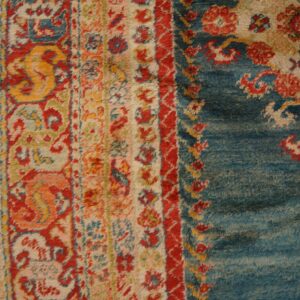High-pile rug with complex red, yellow, and blue floral motifs rests on distressed wood flooring.