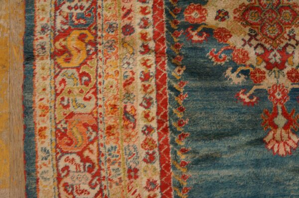 High-pile rug with complex red, yellow, and blue floral motifs rests on distressed wood flooring.
