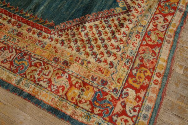 A high-pile rug with red, cream, and teal traditional borders is placed on weathered wood flooring.