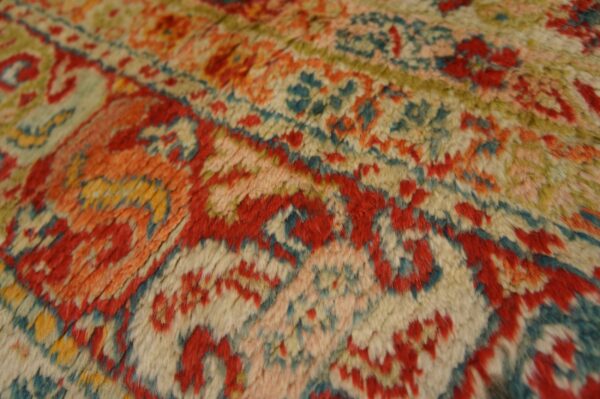 High-pile rug texture closeup featuring a detailed pattern in red, orange, cream, and blue-green.
