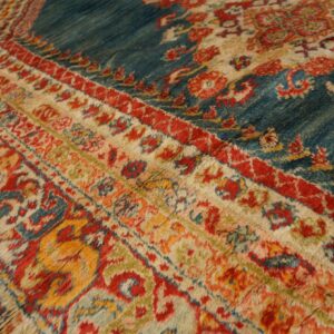 Close-up of a high-pile rug showing red, blue, cream, and gold traditional motifs across the field and striped borders.