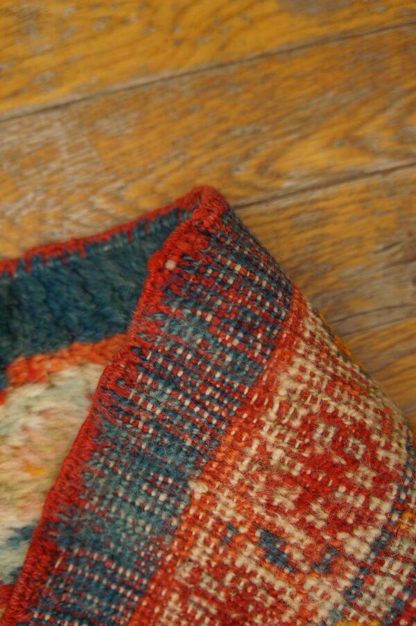 Folded rug edge displaying coarse red, blue, and cream geometric weave against wood flooring.
