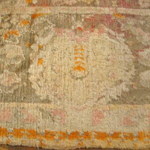 High-pile rug close-up featuring stylized beige, gray, pink, and bright orange designs over wooden flooring.