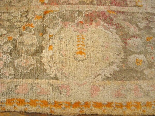 High-pile rug close-up featuring stylized beige, gray, pink, and bright orange designs over wooden flooring.