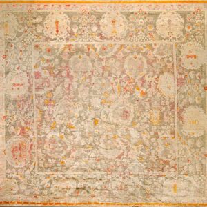 Ornate area rug in muted cream and sage green with faded pink details and an orange border.