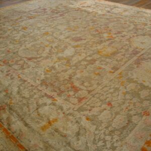A large shaggy tan rug with faded traditional patterns in salmon and bright orange on wood flooring.
