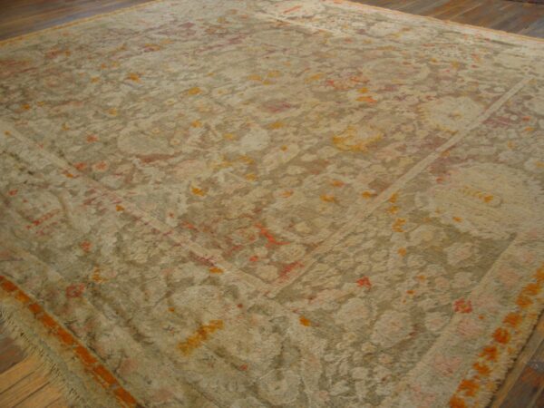 A large shaggy tan rug with faded traditional patterns in salmon and bright orange on wood flooring.