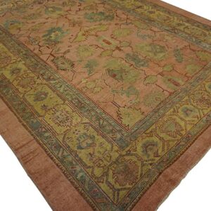 Low-pile rug featuring a rose field with large stylized floral motifs in muted greens and teal.