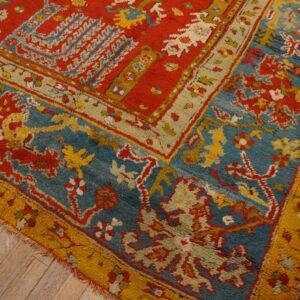 Textured, high-pile rug detail featuring red, blue, and gold traditional patterns over light wood plank flooring.