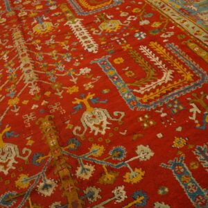 Red rug with ornate yellow, light blue, and white traditional designs and a contrasting wide border.