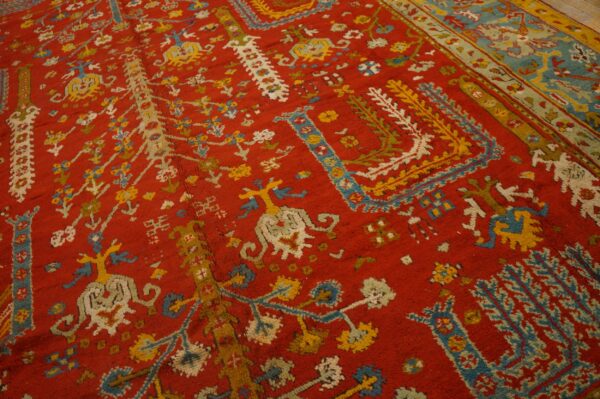 Red rug with ornate yellow, light blue, and white traditional designs and a contrasting wide border.