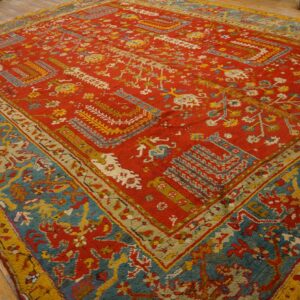 Textured red rug featuring complex teal and yellow designs displayed on natural wood planks.
