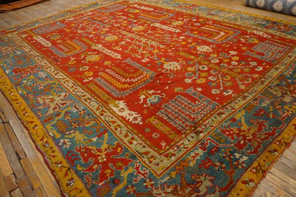 Textured red rug featuring complex teal and yellow designs displayed on natural wood planks.