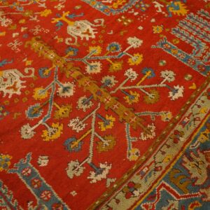 Detail of a red pile rug with traditional blue, yellow, and cream stylized motifs and an olive green border.