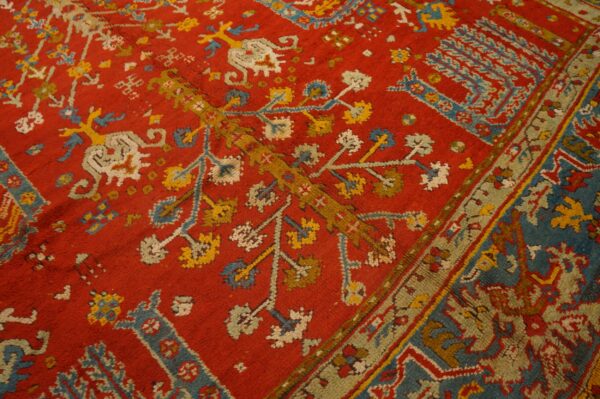 Detail of a red pile rug with traditional blue, yellow, and cream stylized motifs and an olive green border.