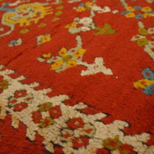 Textured detail of a red high-pile rug featuring stylized floral and geometric motifs in yellow, cream, and blue.