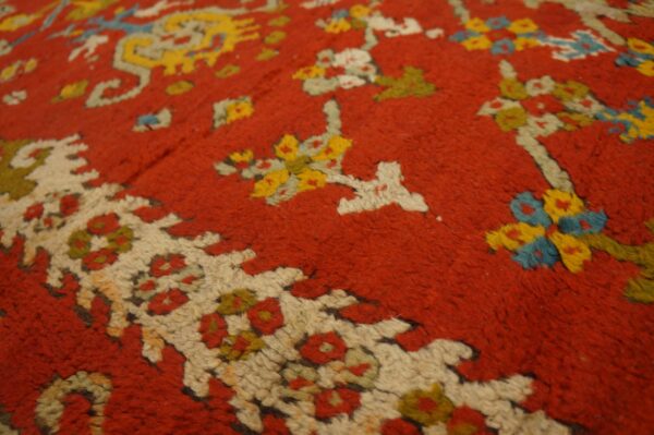 Textured detail of a red high-pile rug featuring stylized floral and geometric motifs in yellow, cream, and blue.